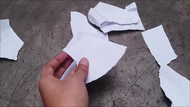 Top view of ripped white paper fragments and shredded waste sheets scattered on a gray concrete industrial background.