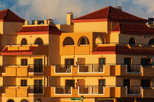 View of a traditional Spanish apartment building with yellow walls, red tiled roofs, and balconies under the warm glow of sunset in Lanzarote, Canarias, Spain.