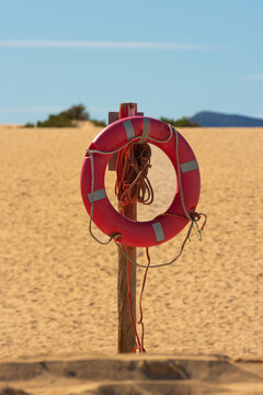 View of a red lifebuoy hanging on a wooden post amidst the vast sand dunes of the Canary Islands under a clear blue sky in Lanzarote, Canarias, Spain.
