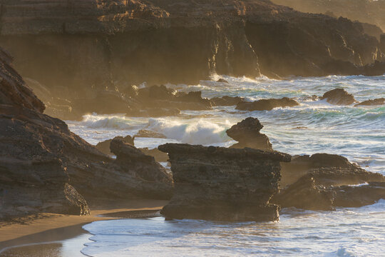 View of rugged volcanic cliffs and crashing waves on a sandy beach during golden hour in Lanzarote, Canarias, Spain.