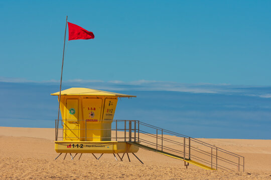 View of a yellow lifeguard tower with a red flag on a sandy beach under a clear blue sky in Lanzarote, Canarias, Spain.