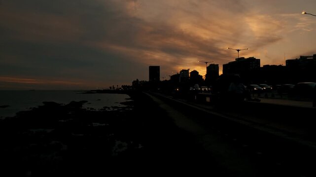 Stunning sunset over a coastal city with cars driving on the rambla. Beautiful golden hour light reflects on the clouds and water