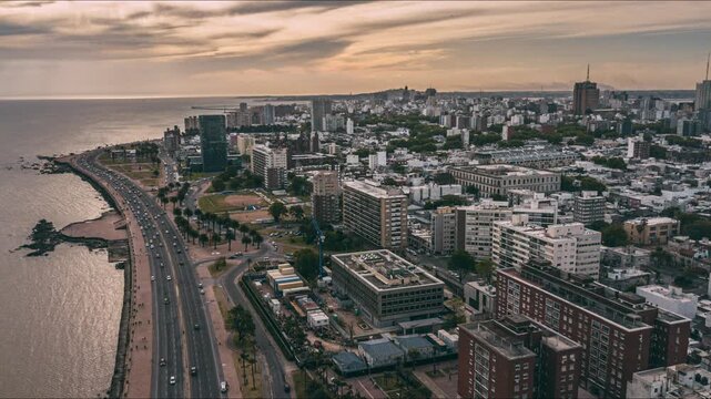 Aerial view flying over the coastal road of montevideo, uruguay. Urban cityscape with buildings, cars, and the rio de la plata at sunset