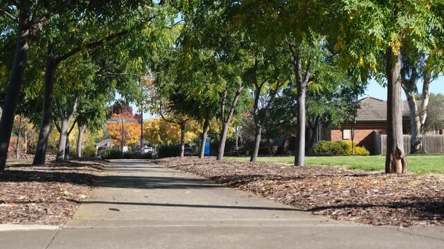 Shaded walking path through a suburban park&nbsp;in Hoppers Crossing, Melbourne Australia. A kid riding a bicycle in distance. A leafy neighborhood green space and family friendly recreational parkland
