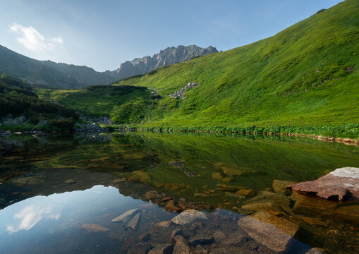View of Bystre pleso mountain lake reflecting lush green slopes and rocky peaks in the Low Tatras National Park Liptovsky Mikulas, Zilinsky kraj, Slovakia.