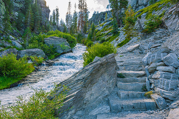 Rustic stone stair steps ascend alongside a fast-flowing mountain cascade through granite boulders and lush green shrubs on a hiking trail in Lassen NP, CA. © ZL Visuals