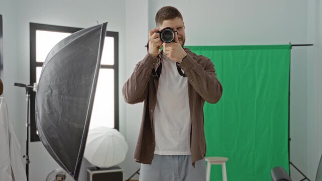 Young man pointing a dslr camera to his eye and reviewing images in a studio, hand on lens while smiling; focused creativity.