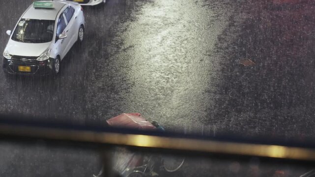 Cyclo driver covered in plastic rides through heavy rain on flooded Hanoi street at night with dramatic lighting and reflections