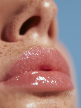 a detailed profile image of a person's lower face, showcasing a tan nose with visible freckles and a puckered mouth with glossy