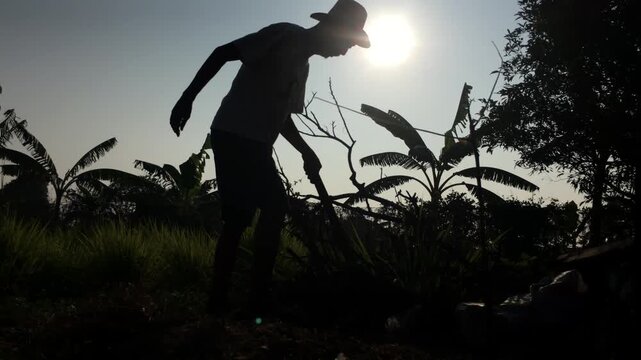 old man is chopping a log to prepare firewood in a rural settlement, silhouetted against the sky.
