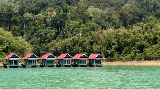 Floating raft houses on the turquoise Cheow Lan Lake in Khao Sok National Park. Traditional eco-friendly accommodation surrounded by lush jungle and limestone mountains in Southern Thailand.