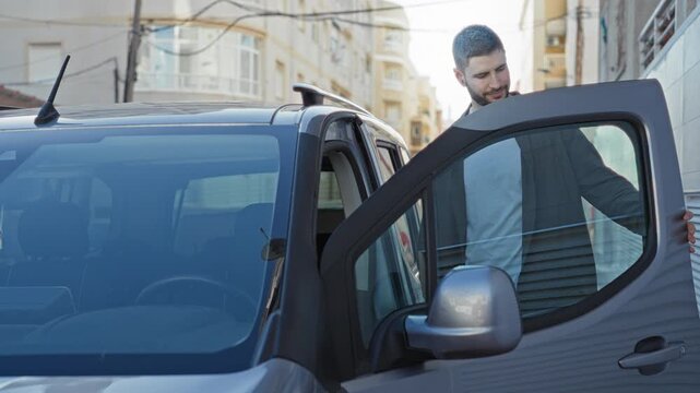 Young hispanic man leans on van door with hand on open door while smiling on a narrow city street; friendly casual commute.