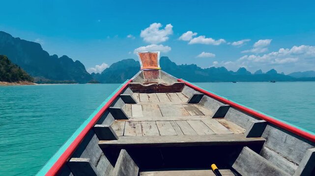Peaceful boat journey across the emerald Cheow Lan Lake in Thailand. Traditional long-tail boat cruising through the majestic limestone mountains and pristine nature of Khao Sok National Park.