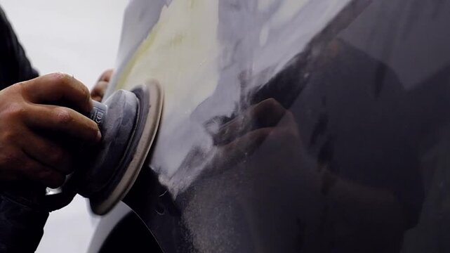 Car polishing process in auto repair shop, worker using orbital sander on vehicle body