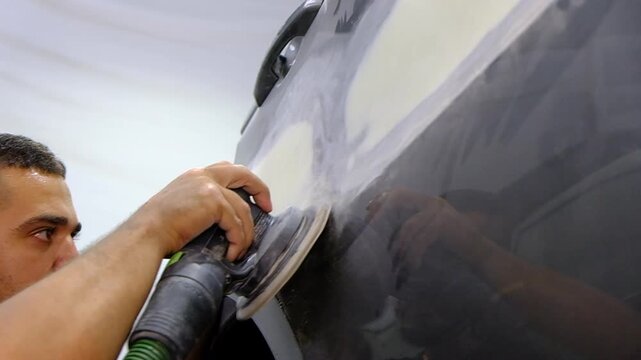 Car polishing process in auto repair shop, worker using orbital sander on vehicle body