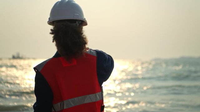 Female engineer at an oil refinery pointing direction and coordinating operations near a coastal energy facility