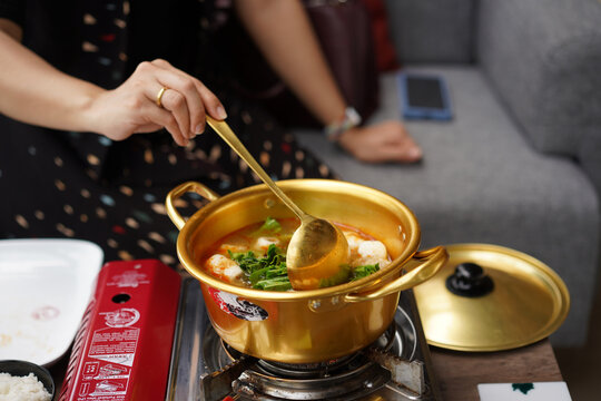 Person stirring hot spicy soup with fish balls and vegetables in kitchen