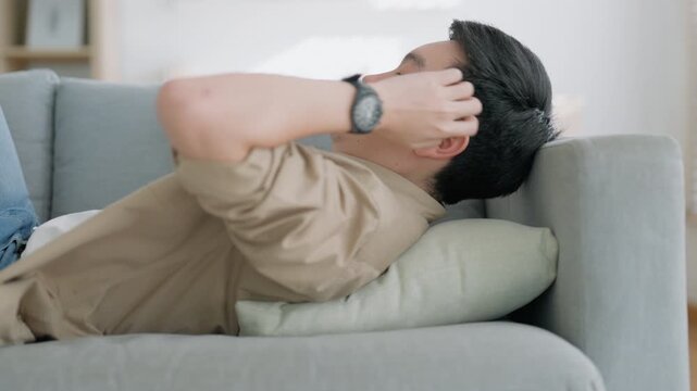 Relaxed young Asian man enjoying rest on comfortable sofa, calm attractive male relaxing on couch
