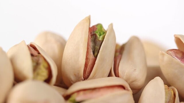 Pile of roasted pistachios in shells rotating slowly on white background. Close-up shot