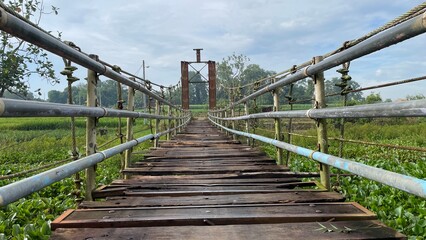 Fototapeta premium Rustic Suspension Bridge Over Water with Wooden Structure and Scenic Natural Landscape View