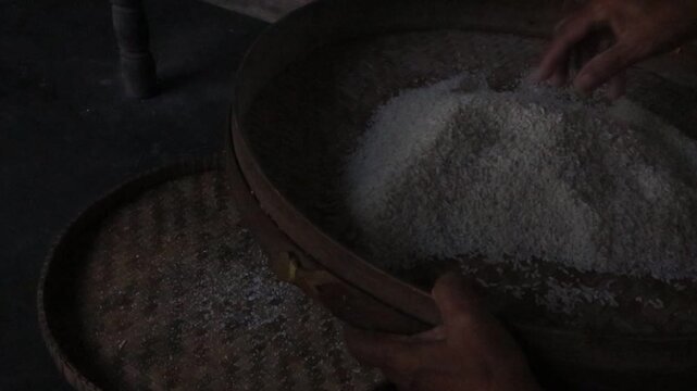 the Asian woman's hands separating rice with dirt such as small pebbles and other dirt before cooking it with a bamboo woven tray, cooking preparation