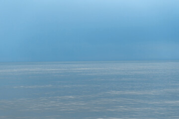 Fototapeta premium A tranquil minimal seascape of a calm blue ocean meeting a soft pale sky at the horizon, evoking serenity, openness and quiet reflection ideal for backgrounds, meditation, wellness and design.