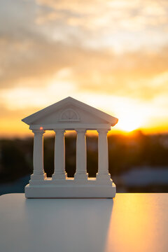 Bank building model with classical pillars against a beautiful sunset sky. Finance, law, and justice icon for banking, real estate investment, or legal services in a professional commercial style.