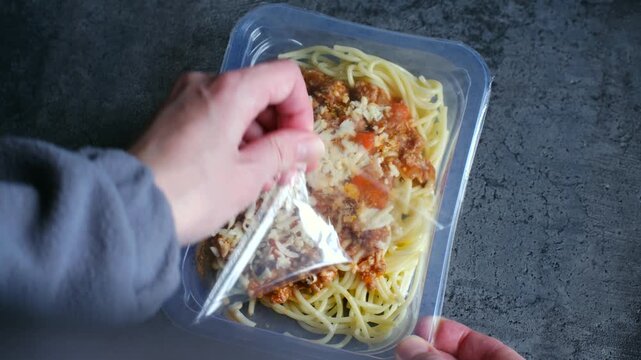 Hands opening plastic container with pre packaged spaghetti bolognese ready meal for quick and convenient lunch or dinner, showing concept of modern fast food and meal delivery
