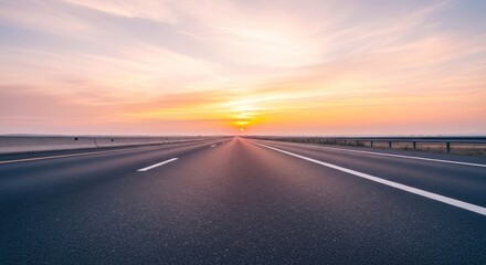 Fototapeta premium An empty highway stretches into the distance, with a vibrant sunset in the background, casting a warm glow over the scene.