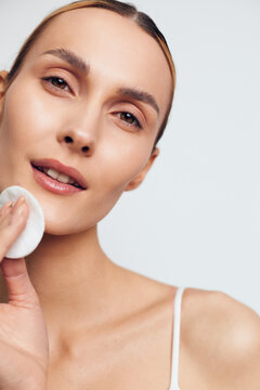 Young woman skincare routine close up she holds cotton pad on cheek gentle cleansing on clean light background fresh natural beauty look at home calm expression makeup free hygiene spa mood