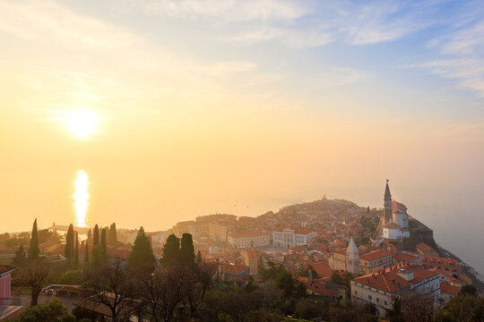 View of the historic old town of Piran with its red-roofed buildings and St. George's Parish Church at sunset in Slovenia.