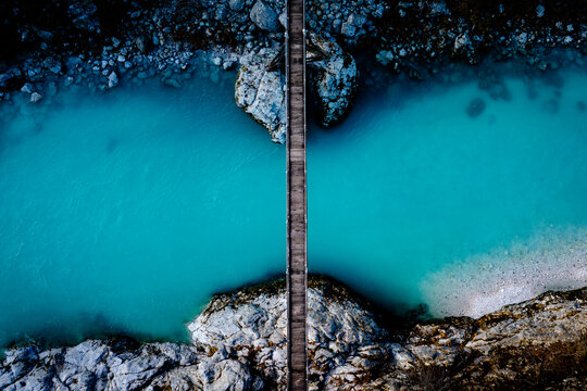 View of a narrow wooden footbridge crossing the vibrant turquoise waters of the Soca river between rocky banks in Slovenia.