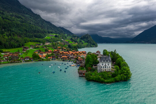 Aerial Drone View of Iseltwald Village on Turquoise Brienzersee Lake | Historic Castle Peninsula, Swiss Chalets and Moody Cloudy Summer Sky in Bernese Oberland
