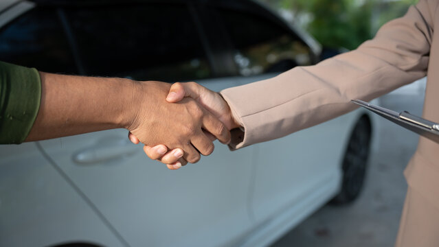 Close-up handshake between two people next to a white car, suggesting agreement during vehicle sale or service transaction, outdoor daylight, shallow depth of field.