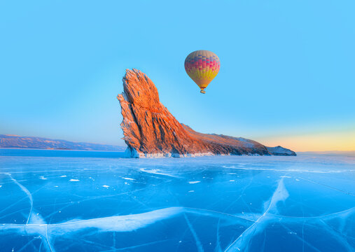 Hot air balloon flying over Ogoy island on winter Baikal lake with transparent cracked blue ice at sunrise - Baikal, Siberia, Russia