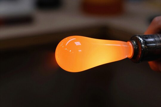 Japanese artisan glowing molten glass on blowpipe end, close-up macro