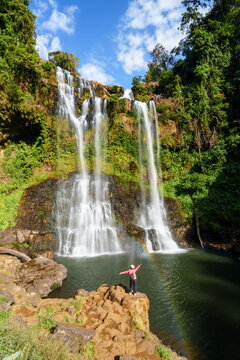 Young female tourist enjoying a beautiful waterfall with a rainbow at Tad Gneuang in Southern Laos