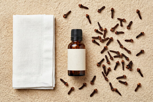 Amber essential oil bottle mockup on light beige textured background with whole dried cloves and linen cloth, natural organic aromatherapy flat lay
