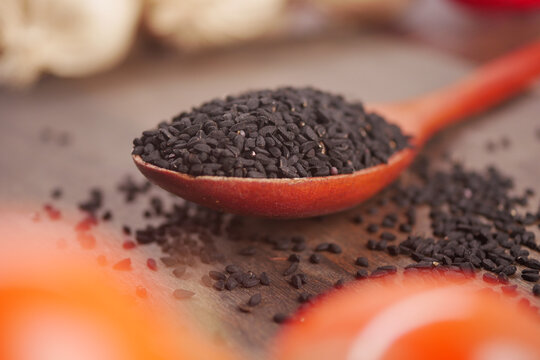 Black cumin seeds on a wooden spoon with blurry background