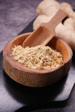 Ginger powder in wooden bowl with scoop on dark surface