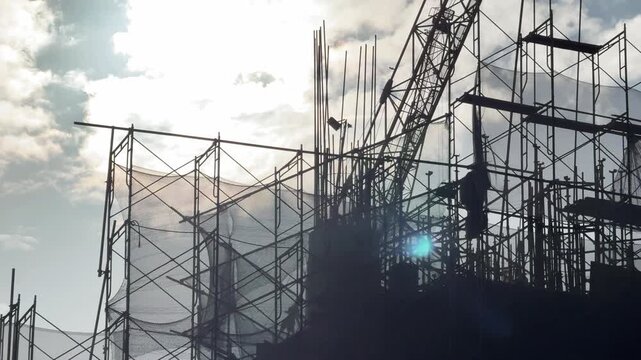 Silhouettes of Construction Scaffolding and crane working Against Cloudy Sky at sunset