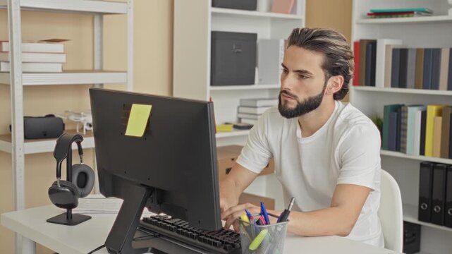 Man points finger to camera at computer desk in an office, smiling while typing and gesturing toward the screen; confidence connection.