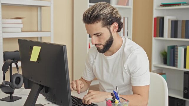 Man typing on desktop computer with fingers on keyboard, headphones on stand, at desk in studio; concentration productivity.