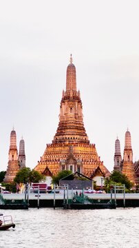Wat Arun Ratchawararam in Bangkok, Thailand, with a bright golden orange sunset as the backdrop. The reflection of the temple on the water below creates a peaceful and elegant atmosphere.