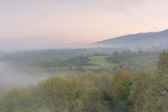 View of the Balze del Valdarno landscape with misty hills and lush green trees under a soft morning sky in Piantravigne, Tuscany, Italy.