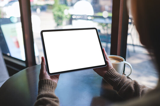 Mockup image of a woman holding digital tablet with blank white desktop screen in cafe