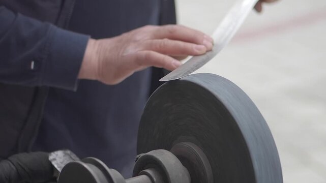 Man sharpens knife with grinding wheel in workshop