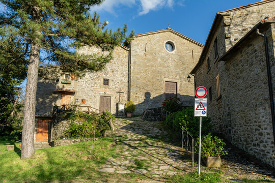 View of the historic stone church and ancient village buildings with a cobblestone path and lush greenery under a blue sky in Loro Ciuffenna, Tuscany, Italy.