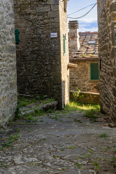 View of a narrow stone alleyway with historic buildings, green shutters and terracotta tiled roofs in the medieval village of Loro Ciuffenna, Tuscany, Italy.