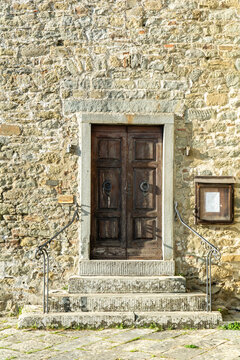 View of an ancient wooden double door with iron knockers set in a rustic stone wall with steps and handrails in the historic village of Loro Ciuffenna, Tuscany, Italy.